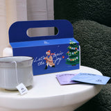 Blue gift box with a design featuring tea bags, cup and Christmas tree on a white surface.